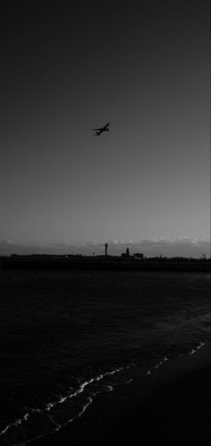 an airplane is flying over the water at sunset or sunrise, black and white photo