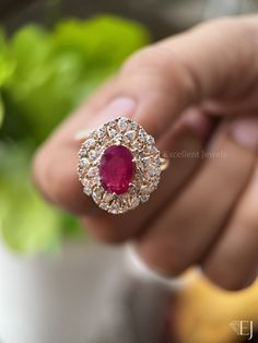 a close up of a person's hand holding a ring with a red stone