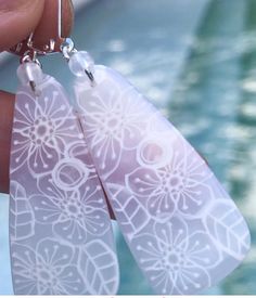 a pair of earrings with white paper cut outs and flower designs hanging from silver earwires