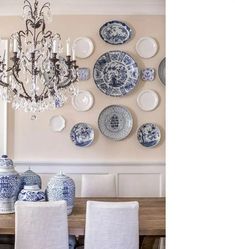 a chandelier hangs above a dining room table with blue and white plates on the wall