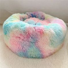 a multicolored round dog bed on a white carpet in the corner of a room