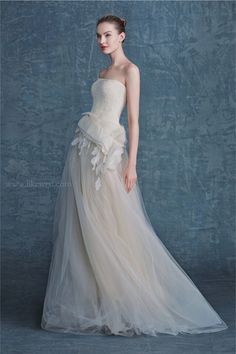 a woman in a wedding dress standing against a blue wall with her hands on her hips