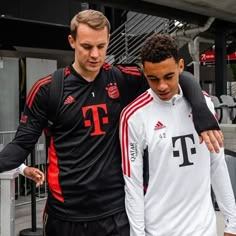 two soccer players are walking together in front of the stands and one is holding his arm around another player's shoulder