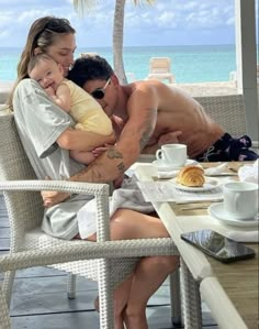 a man and woman hugging each other while sitting at a table in front of the ocean