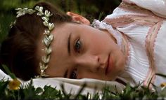 a woman laying in the grass wearing a white dress and headband with flowers on it