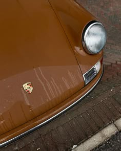 the front end of a brown porsche parked on a brick sidewalk next to a red fire hydrant