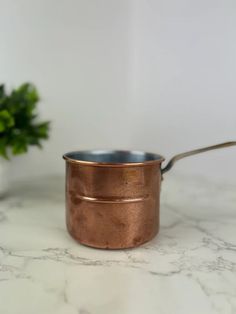 a small pot with a spoon in it sitting on a counter top next to a plant