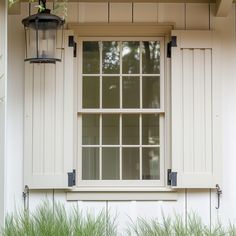 a lamp hanging from the side of a house next to a window with shutters