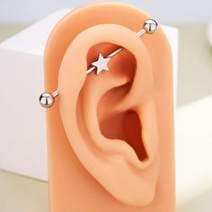 an ear with two silver balls and a star on the middle, is shown in front of a white box