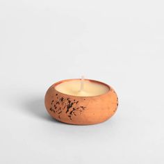 a candle that is sitting inside of a wooden bowl on a white surface with black spots