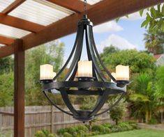 an outdoor chandelier hanging from a wooden pergolated roof over a yard