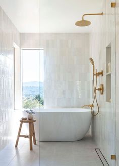 a white bath tub sitting next to a walk in shower under a window with a wooden stool