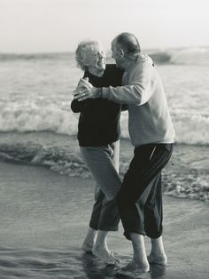 an older man and woman hugging on the beach