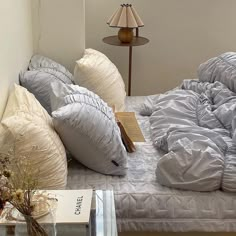 a bed with many pillows on top of it and a lamp next to it in the corner