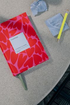 a red notebook sitting on top of a table next to a yellow pen and paper