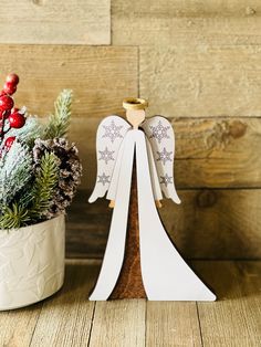 an angel statue next to a potted plant with pine cones and berries on it