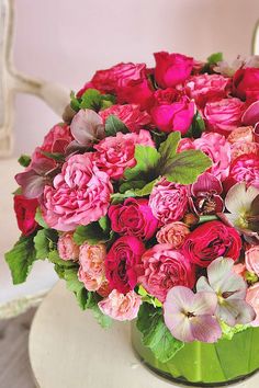 a green vase filled with lots of pink and red flowers on top of a table