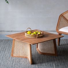 two wicker chairs and a coffee table with fruit on it in front of a white wall