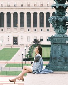 a woman sitting on the edge of a fountain in front of a building with columns