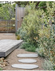 a wooden deck in the middle of a garden with stepping stones and plants around it