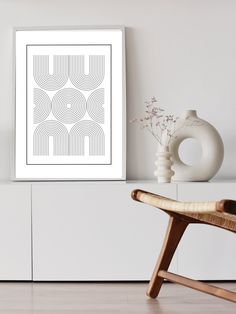 a white framed art print sitting on top of a wooden chair next to a vase