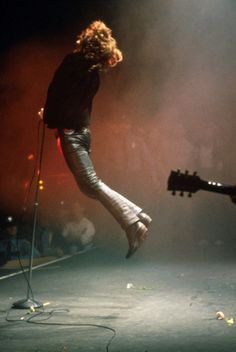 a person jumping in the air on stage with a guitar and microphone to their side