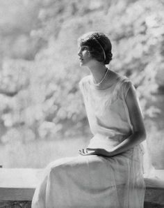 a black and white photo of a woman in a dress sitting on a window sill