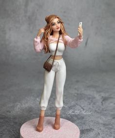 a figurine holding a cell phone in her right hand and wearing white pants