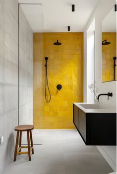 a bathroom with yellow tiles and a stool in front of the shower area is shown