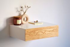 a wooden shelf with a vase, candle and other items on it next to a white wall