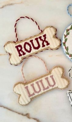 three cross stitch ornaments on a marble surface with the word roux written across them