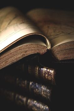 an open book is sitting on top of three old books, with the pages turned upside down