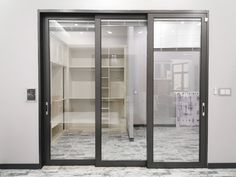 an empty walk - in closet with glass doors and shelves on the wall, next to a tiled floor