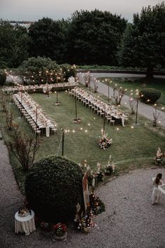 an outdoor wedding setup with white tables and candles on the lawn, surrounded by greenery