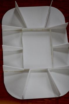 an empty white paper plate on a wooden table with several sections cut out to form a square