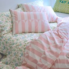 a bed covered in pink and white sheets next to two pillows on top of each other