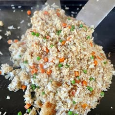 rice with peas and carrots is being cooked on a black plate next to a knife