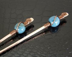 two blue beads are attached to copper wire on a black surface, with the bead in place