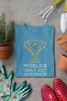 a blue shirt that says world's okayest gardener next to gardening tools and flowers