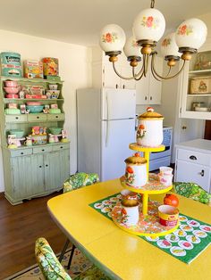 a yellow table with plates and cups on it in a kitchen next to a white refrigerator