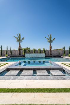 an empty swimming pool surrounded by grass and palm trees on a clear blue sky day