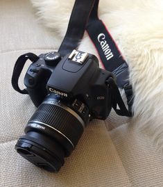 a camera sitting on top of a couch next to a strap that has the word canon written on it