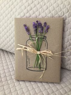 a card with lavender flowers in a mason jar tied to twine on top of a bed