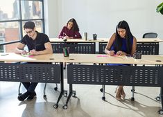 three people sitting at desks in an office setting with papers and pens on them