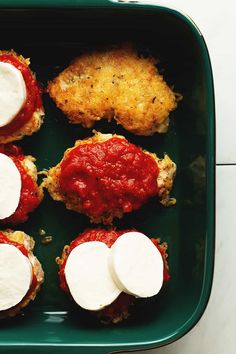 four mini pizzas with cheese and sauce in a green dish on a white table