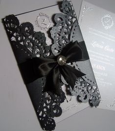 a black and white wedding card with a bow on it's side, sitting next to an envelope