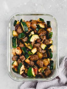 a glass dish filled with meat, vegetables and potatoes on top of a gray towel