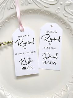 two white tags with black ink on them are sitting on a plate, one has a pink ribbon