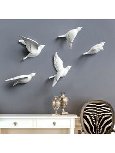 white birds are flying in the air above a table and zebra print chair, on a gray wall