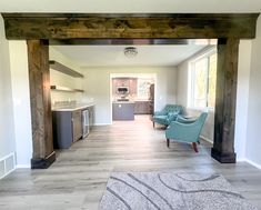 an empty living room and kitchen area with wood beams on the ceiling, hardwood flooring, and blue chairs